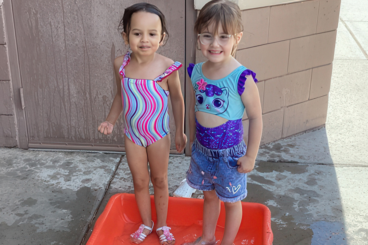 Two happy young girls in swimsuits playing in a red tub with water at ElevateChild Scottsdale, AZ.