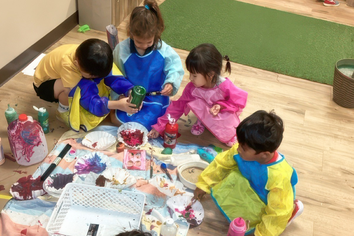 Children in smocks doing a messy art project on the floor in a Reggio Emilia inspired preschool in Scottsdale, Arizona.
